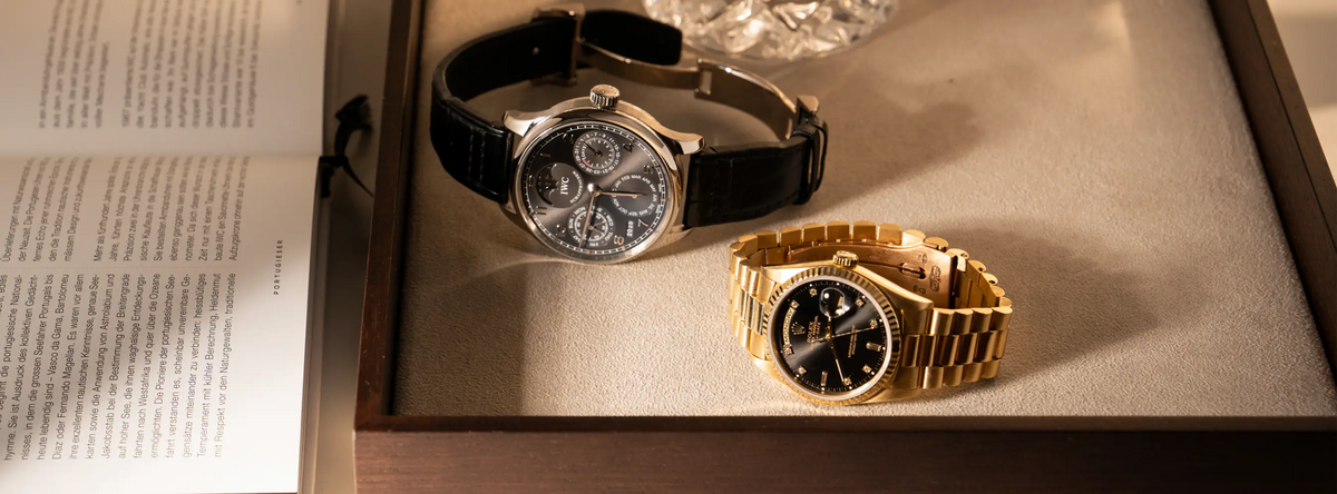 Rolex Day-Date 36 der Referenz 18238 in Gelbgold mit schwarzem Diamant-Zifferblatt liegt neben einem IWC Portugieser Perpetual Calendar in Weißgold mit einem antrazitfarbenem Zifferblatt auf einem Juweliers-Tablet
