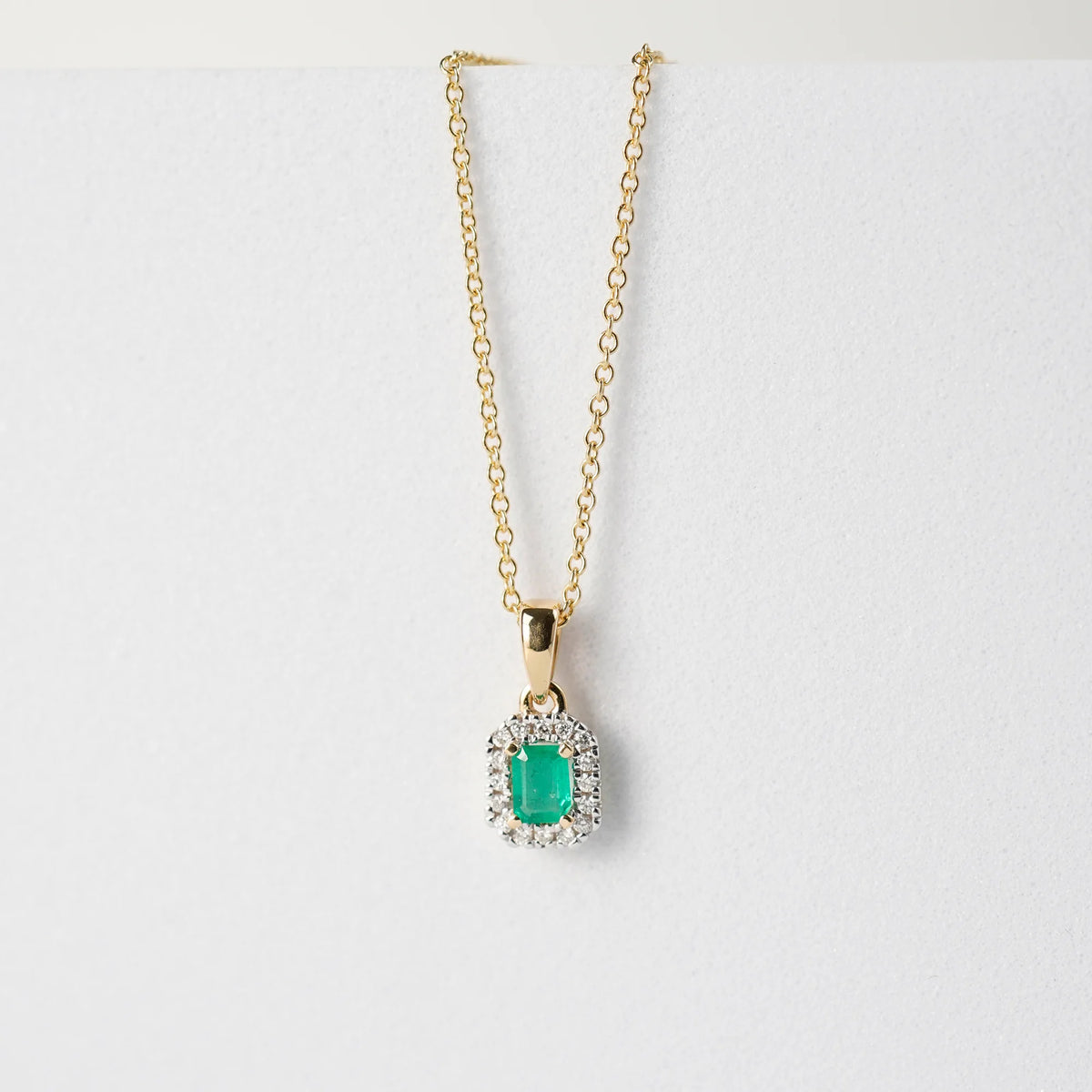 Produktfoto des Anhängers mit einem zentralen Smaragd mit einer kräftigen grünen Farbe, der von kleinen Diamanten umrandet ist, von der Smaragd-Brillant-Kette aus der Schmuckatelier Lang Collection zusammen mit der gelbgoldenen Kette