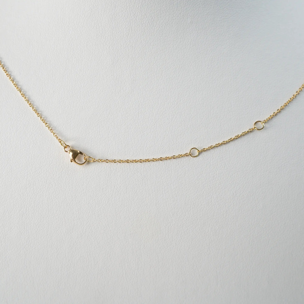 Detailaufnahme der gelbgoldenen Kette und deren Verschlussmechanismus, bestehend aus einem Karabiner und drei eingearbeiteten Ösen in der Kette, um die Länge in drei Einstellungen variieren kann