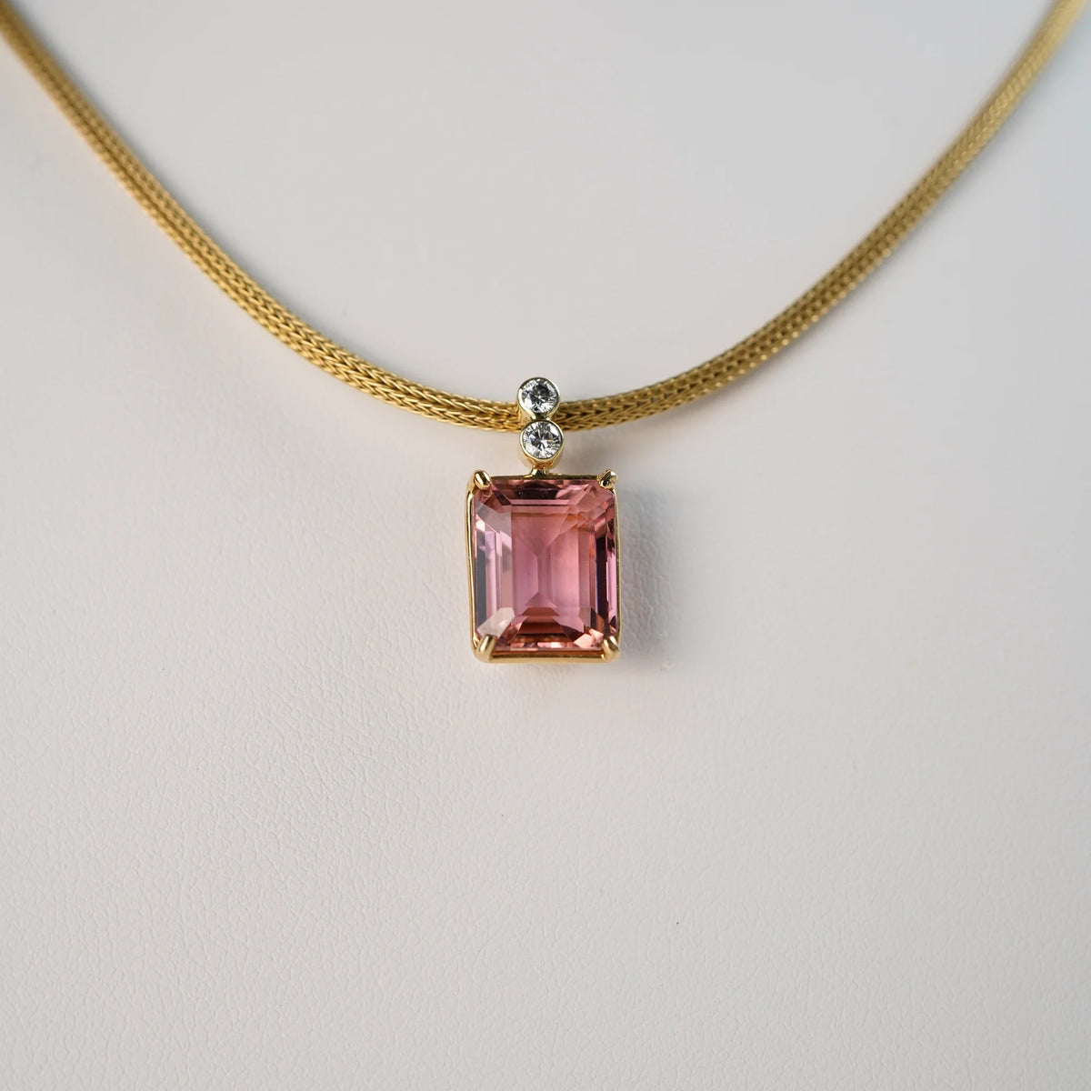 Detailaufnahme des Anhängers des Colliers mit einem großen pinken Tansanit in einer Gelbgold-Fassung und zwei Brillanten als Verzierung der Öse