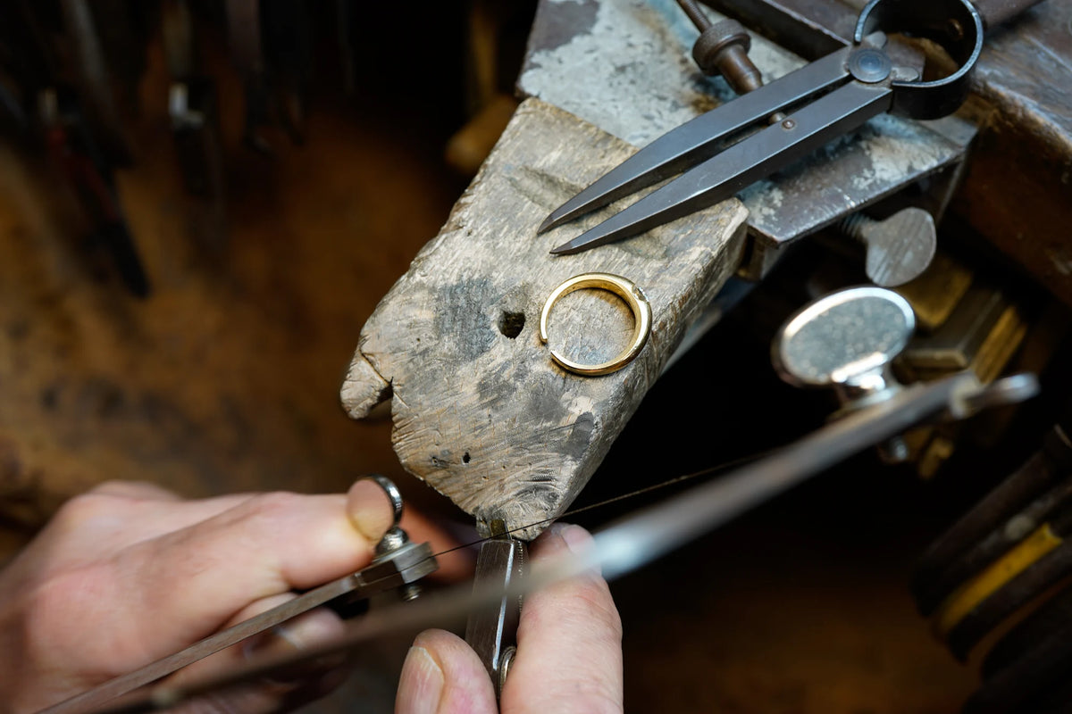 Goldschmied sitzt an seinem Arbeitsplatz und sägt ein Stück Gold zu recht um einen Ring in der Größe anzupassen