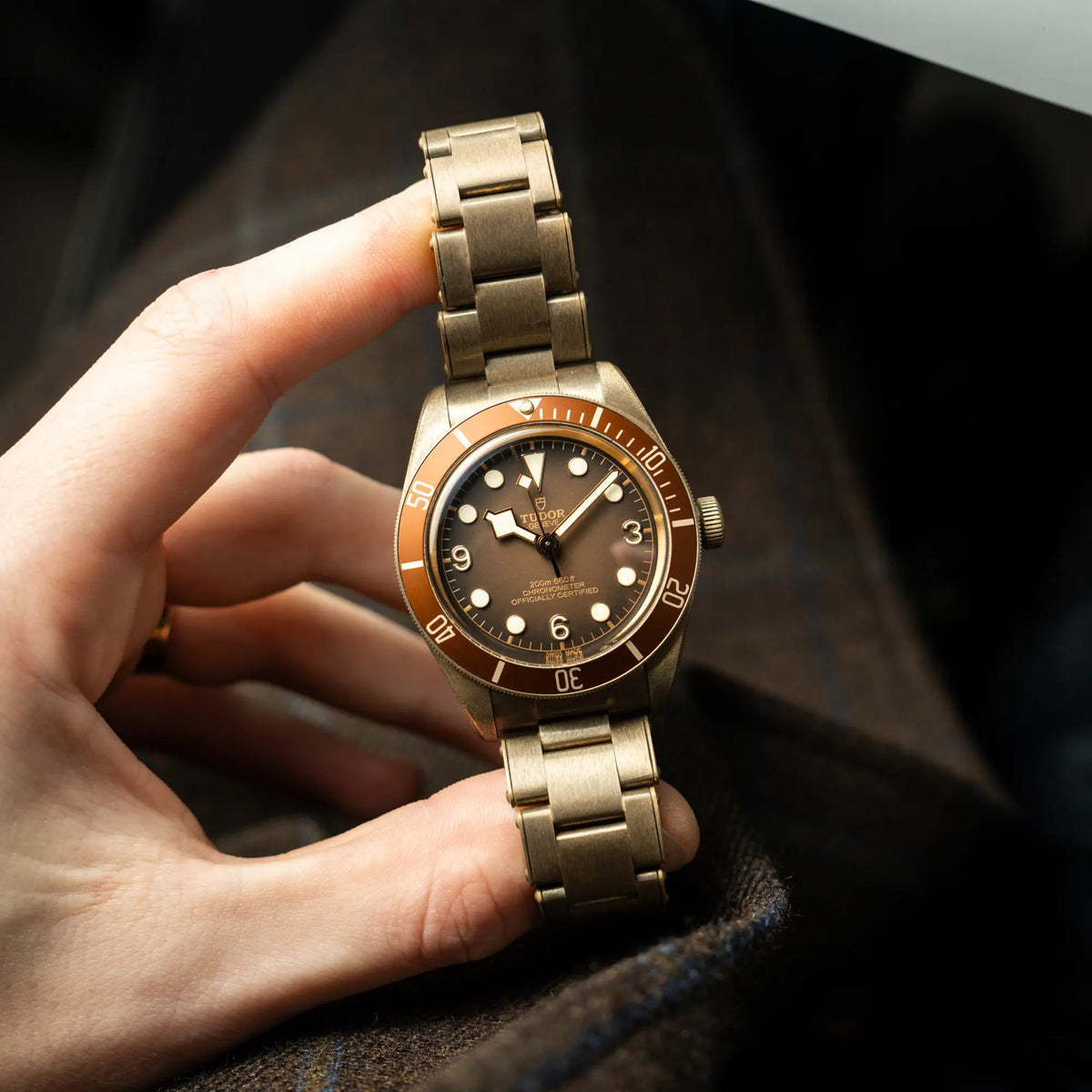 Mann hält die Tudor Black Bay 58 M79012M in Bronze, deren Oberfläche bereits mit einer gleichmäßigen Patina überzogen ist, mit einem braunem Zifferblatt zwischen Daumen und Zeigefinger