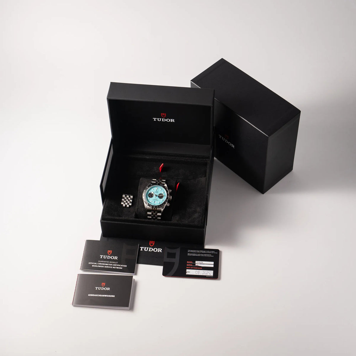 Lieferumfang zugehörig zu der Tudor Black Bay Chronograph Flamingo mit dem türkis-blauen Zifferblatt und schwarzer Lünette mit Zähler-Skala, bestehend aus Box mit Umkarton, originaler Garantiekarte und allen Booklets