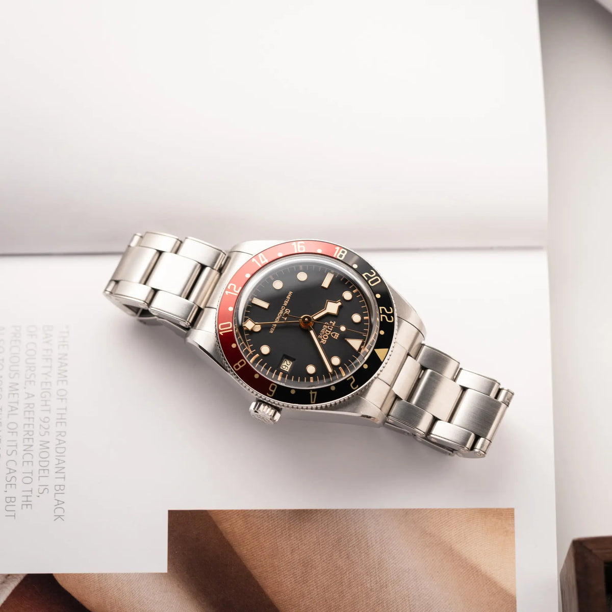 Tudor BlackBay GMT Coke der Referenz 7939G1A0NRU mit der schwarz-roten Lünette und bronzefarbenen Details am Edelstahlarmband  liegt flach auf einem Uhrenbuch