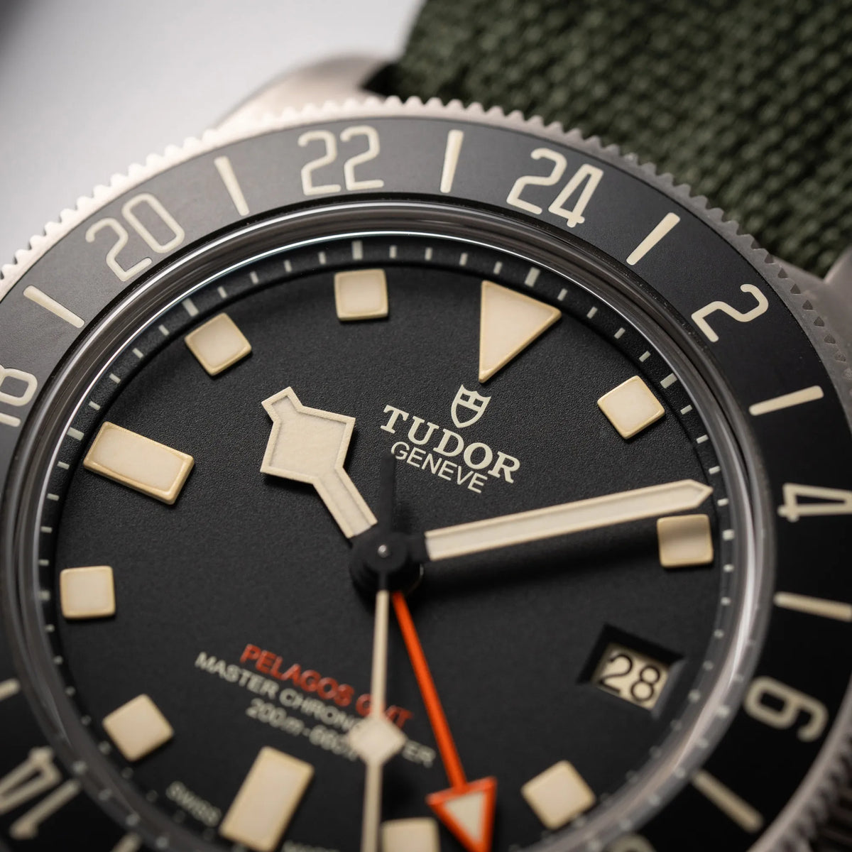 Detailaufnahme der Tudor Pelagos GMT Military der Referenz M2542G257NU-0002 mit Titan-Gehäuse und schwarzem Zifferblatt an einem olivgrünen Nato-Strap fokussiert das Tudor-Logo bei 12 Uhr