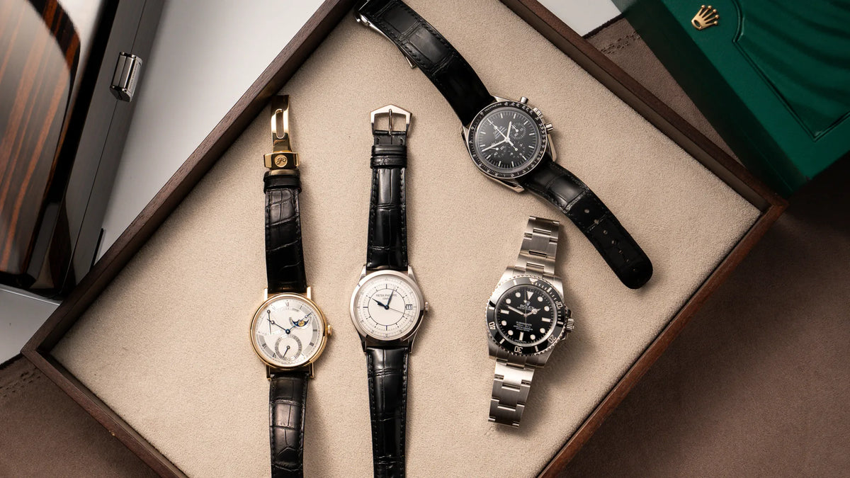 4 exklusive Luxusuhren liegen auf einem Juwelierstablet: eine Breguet Classique in Gelbgold, eine Patek Philippe Calatrava Sector-Dial, eine Omega Speedmaster am schwarzen Lederband und eine Rolex Submariner No-Date in schwarz